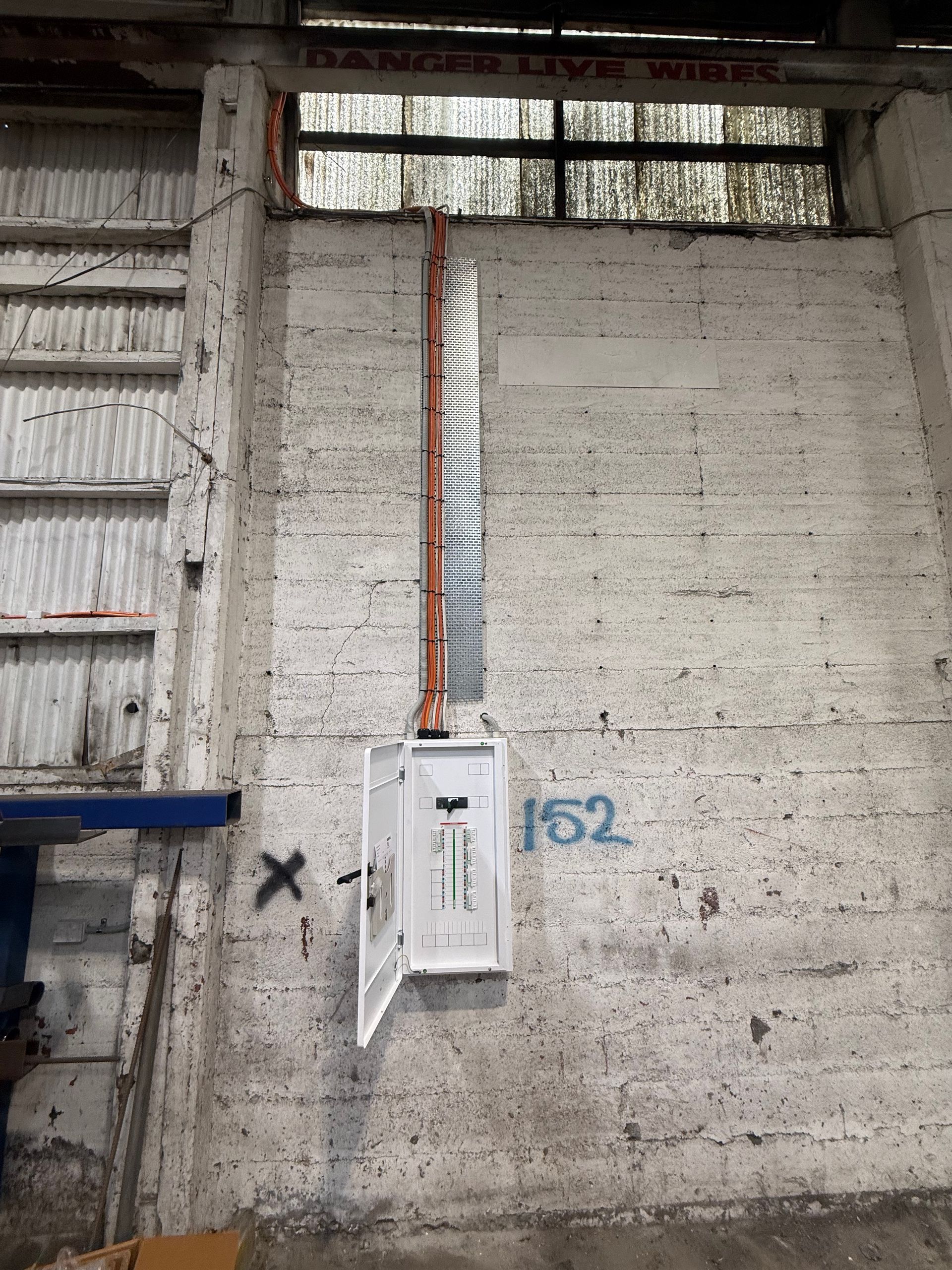 Wall-mounted electrical panel with conduit on a concrete interior wall under a small window.