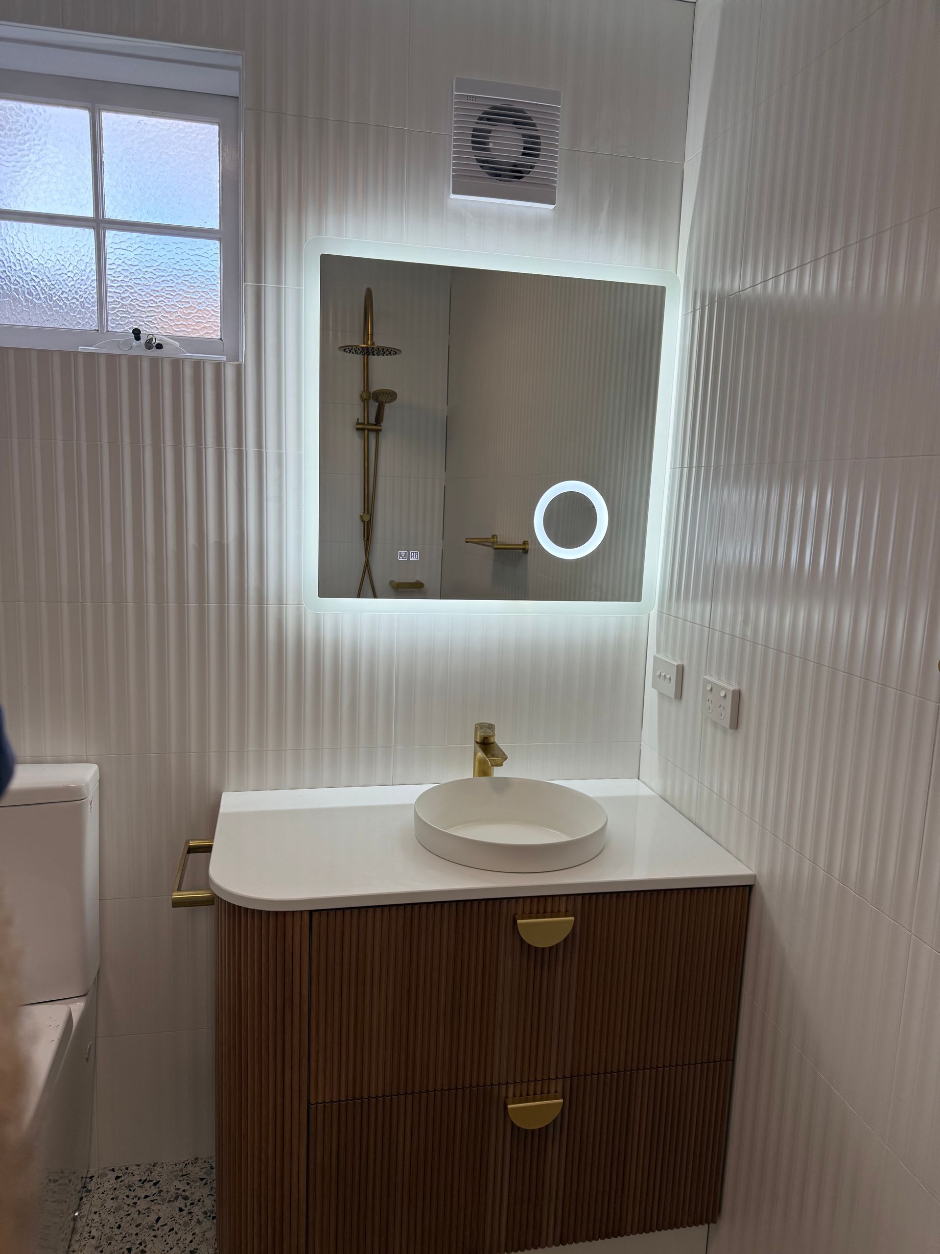 Modern bathroom vanity with sink, mirror, window, and white striped wallpaper.