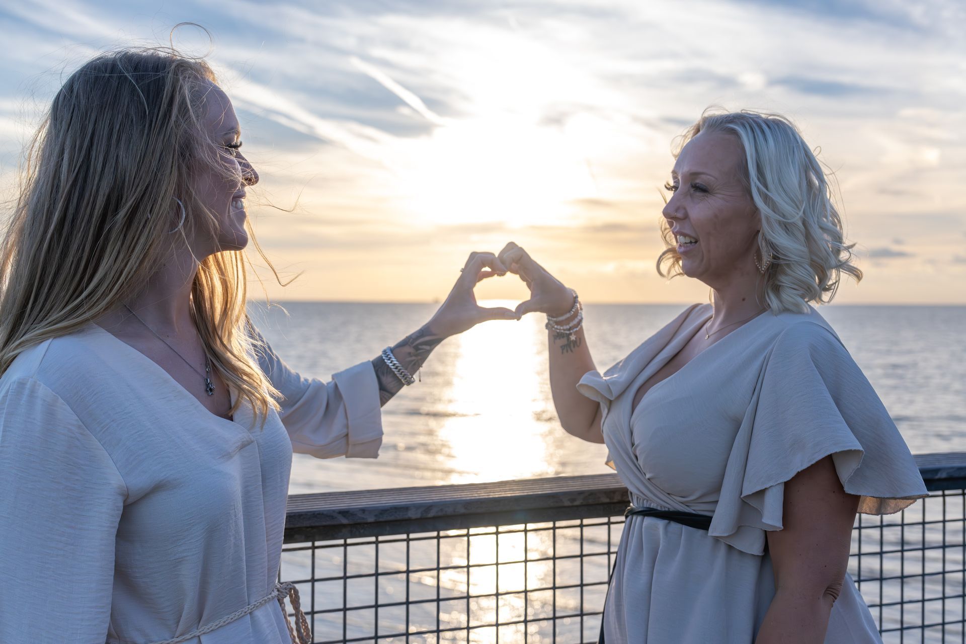 Twee vrouwen klinken met hun glazen bij zonsondergang aan de oceaan, met een heldere horizon op de achtergrond.