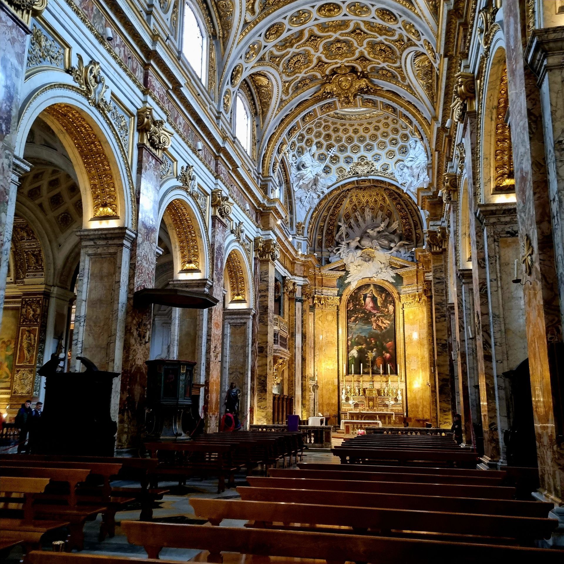 Rijk versierd kerkinterieur met gouden plafonds, gewelfde zuilen en rijen houten kerkbanken.