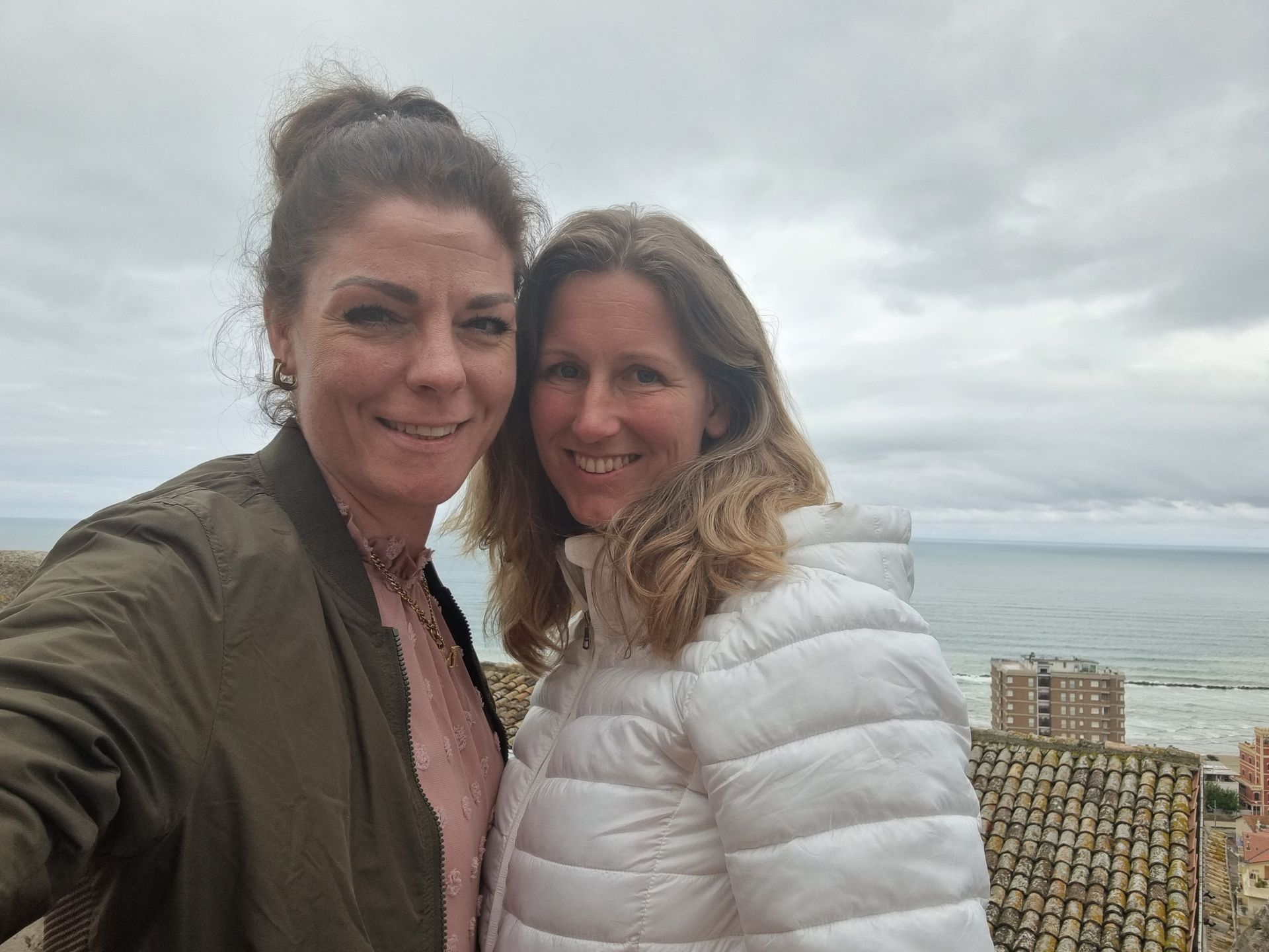 Twee mensen lachend voor een selfie aan de oceaan op een bewolkte dag.