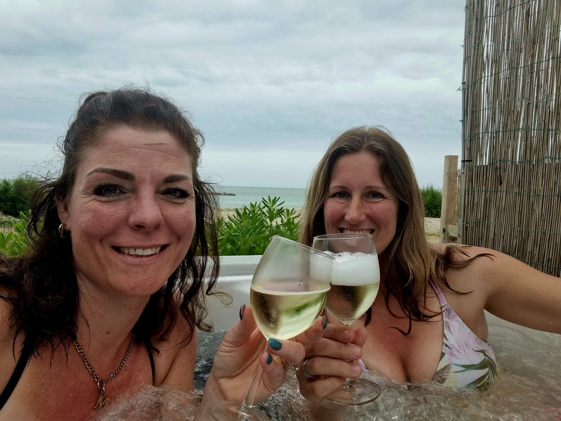 Twee vrouwen glimlachen en proosten met witte wijn in de buitenlucht aan het strand.