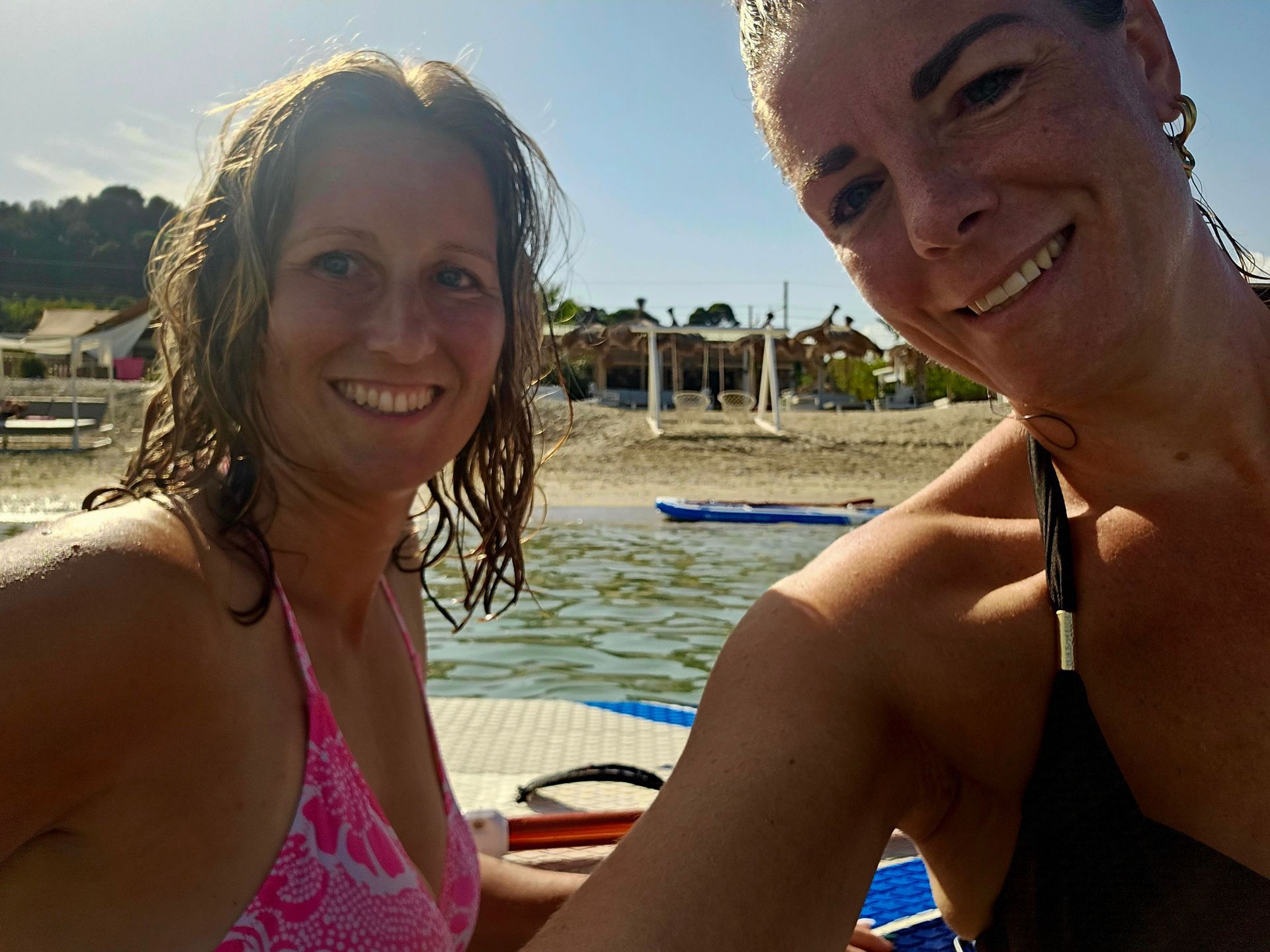 Twee lachende mensen in badkleding maken een strandselfie bij het water.