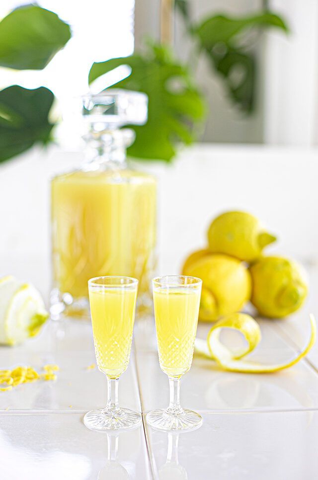 Twee champagneglazen en een karaf gele limonade met citroenen op een vrolijke tafel.