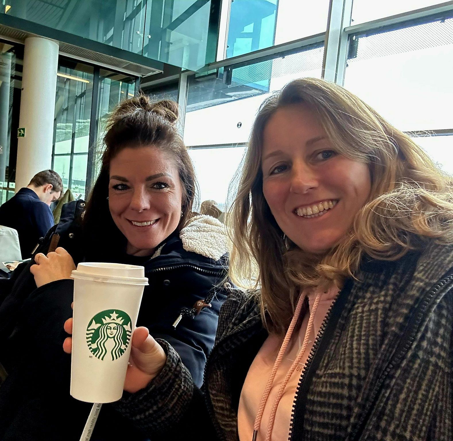 Twee lachende mensen zitten aan een tafeltje bij Starbucks en houden een koffiekopje vast in een lichte caféruimte.