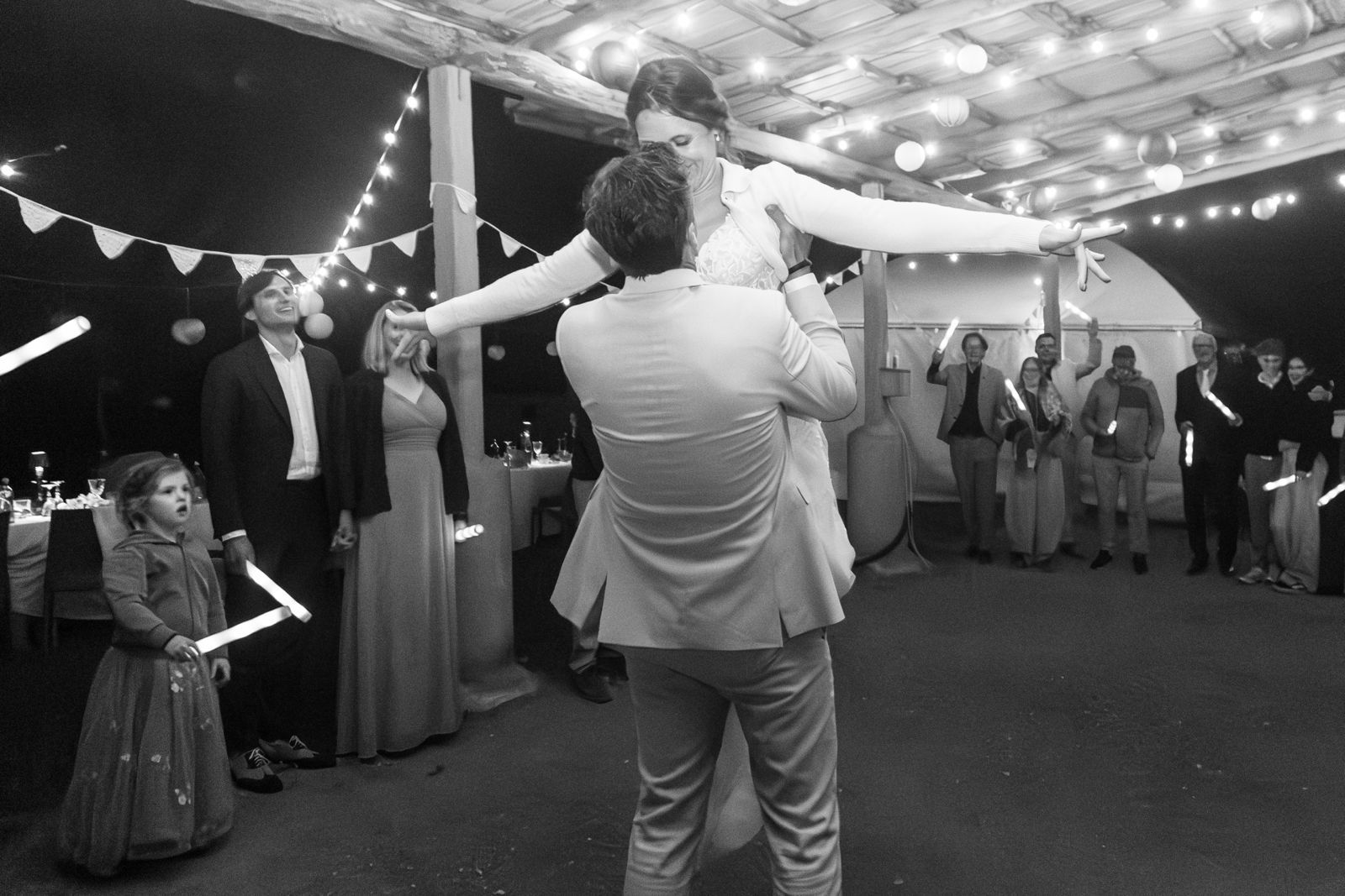 Een stel danst tijdens een formele receptie binnen, terwijl de gasten toekijken onder sfeerverlichting.