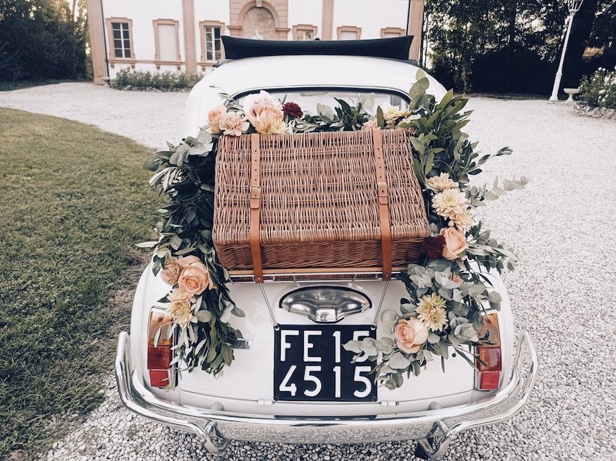 Versierde zilverkleurige auto met bloemen en een rieten mand, van achteren gezien op een oprit.