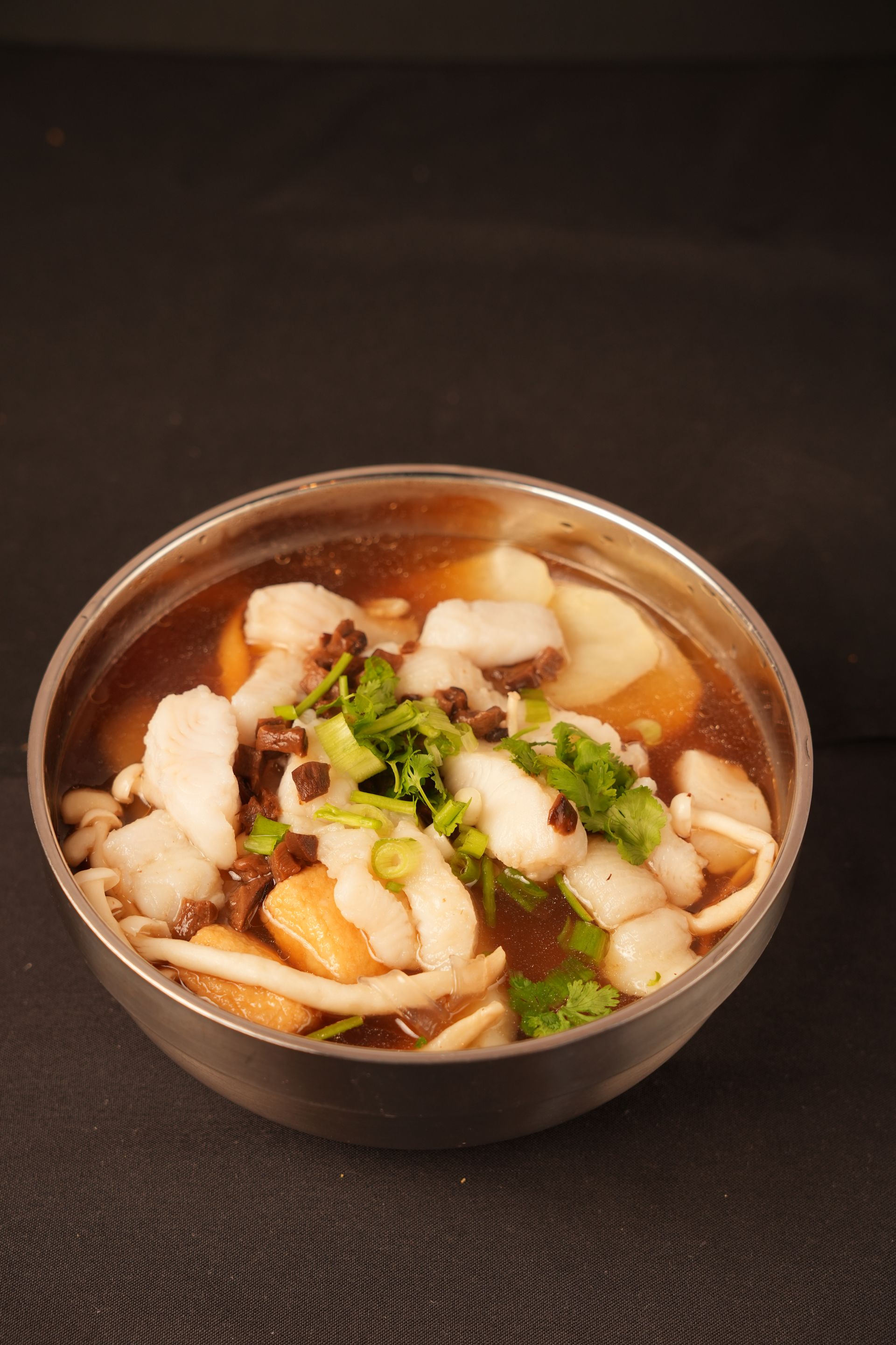 Small bowl of noodle soup with vegetables and herbs on a dark surface