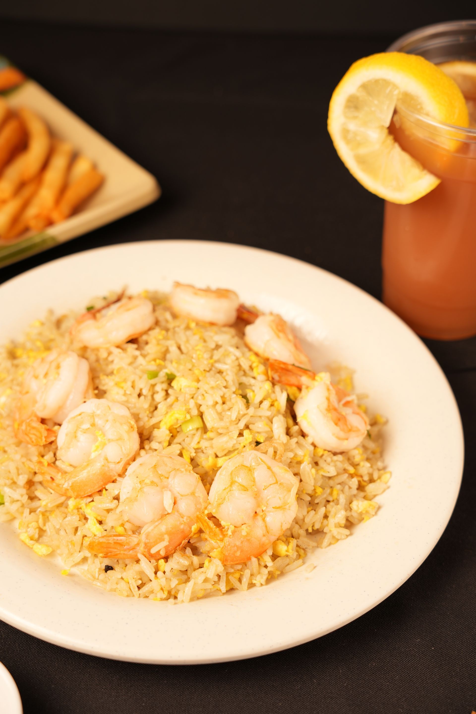 Shrimp fried rice on a white plate beside a cocktail with a lemon garnish