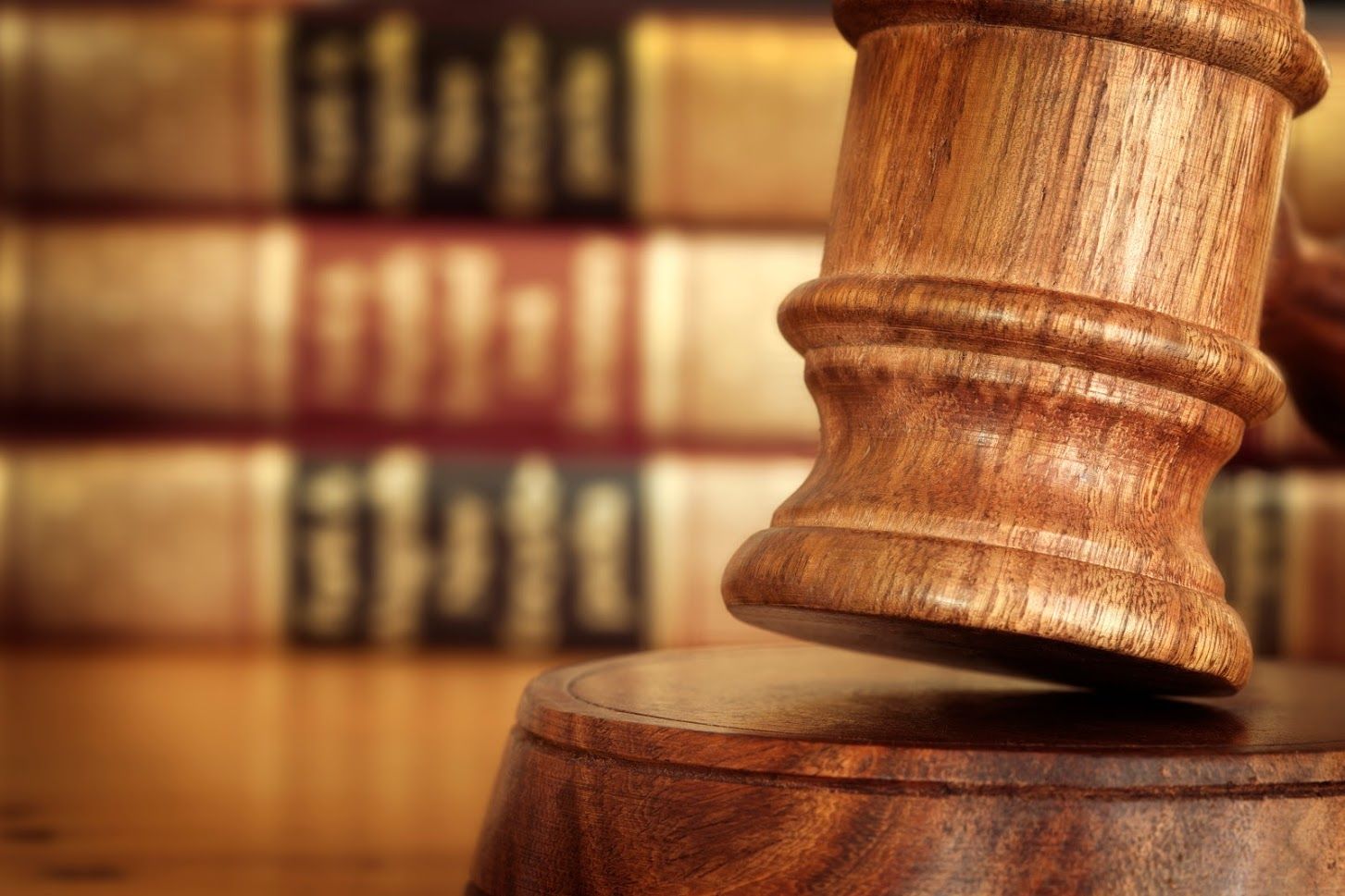 Wooden gavel striking a wooden block, with law books in the blurred background.
