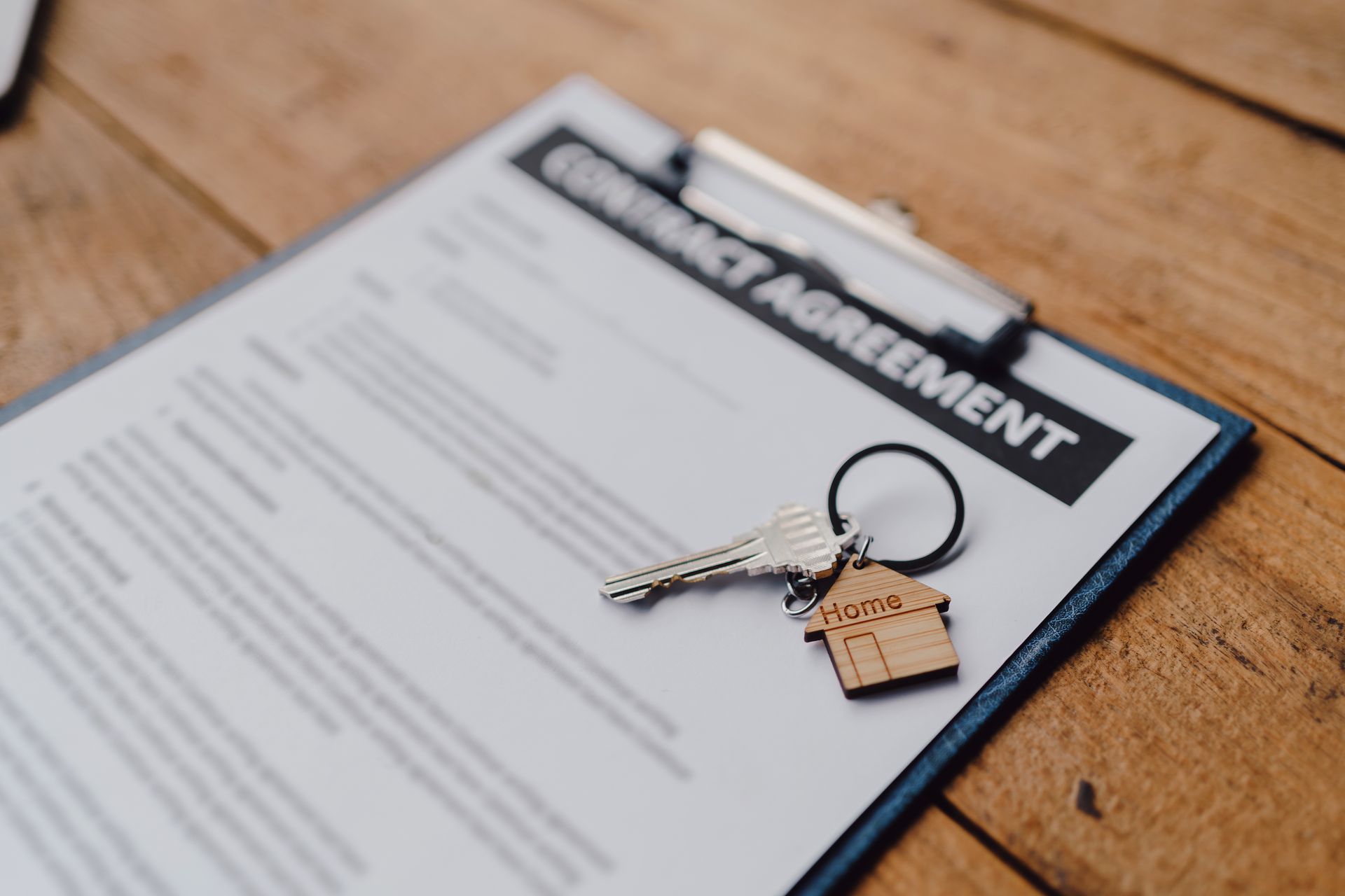 Close-up of a tenancy agreement document with a small house keychain on a wooden table, symbolizing real estate or rental property contract. 