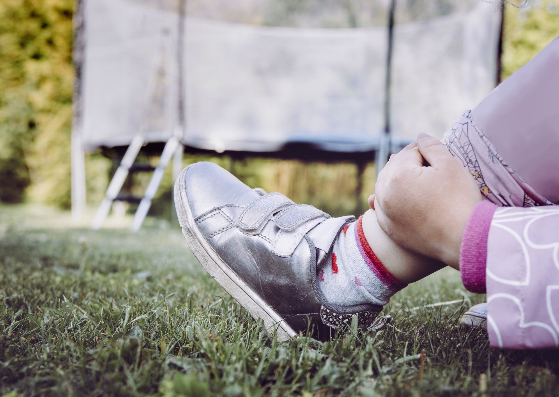 Child's silver shoe on grass, with a trampoline in the background.