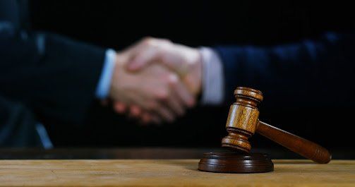 Wooden gavel on a desk, with two people shaking hands in the blurry background.