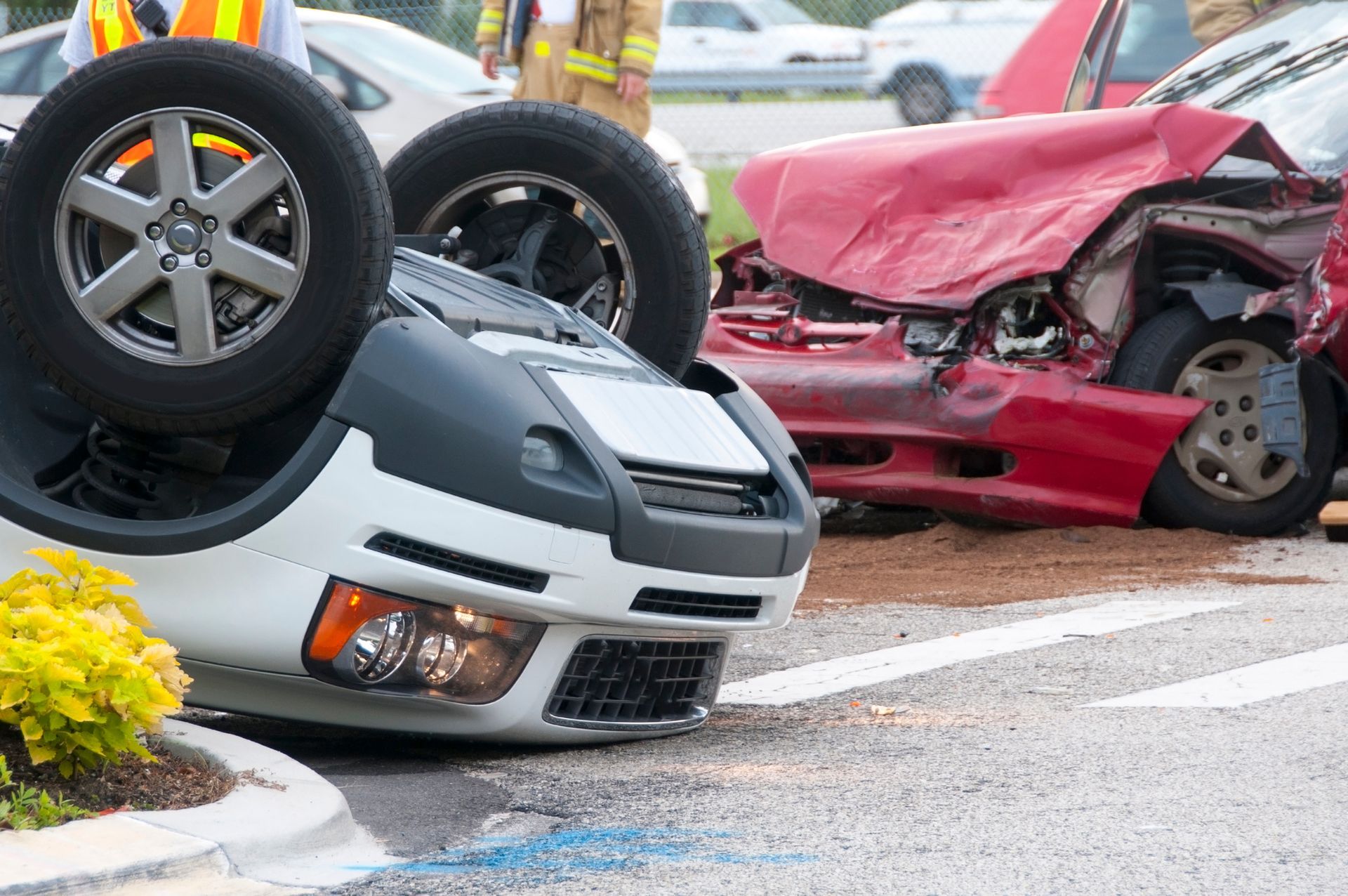 A white car overturned and a red car heavily damaged in a car accident on a road.