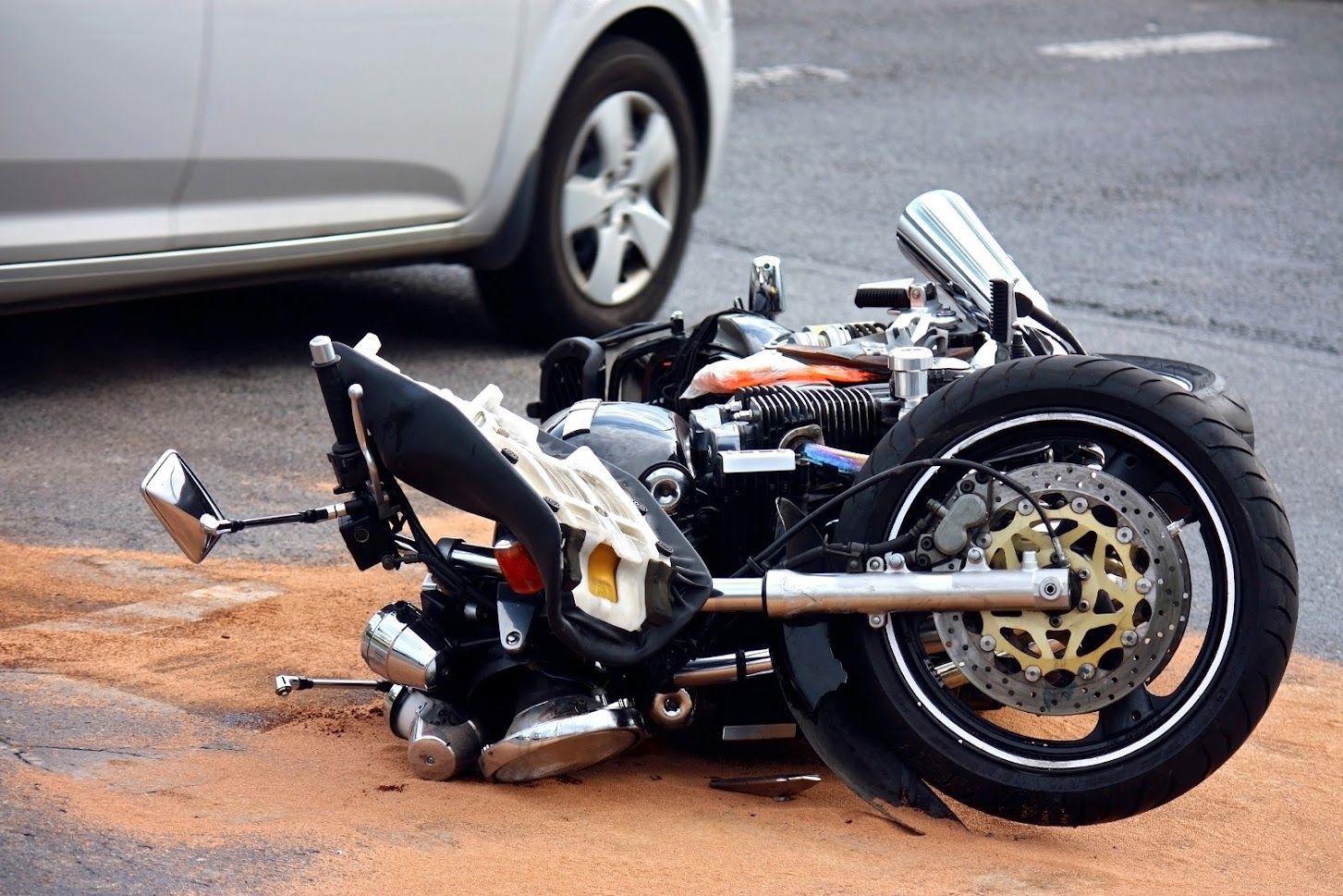 Motorcycle crashed on road next to a car. Debris visible.