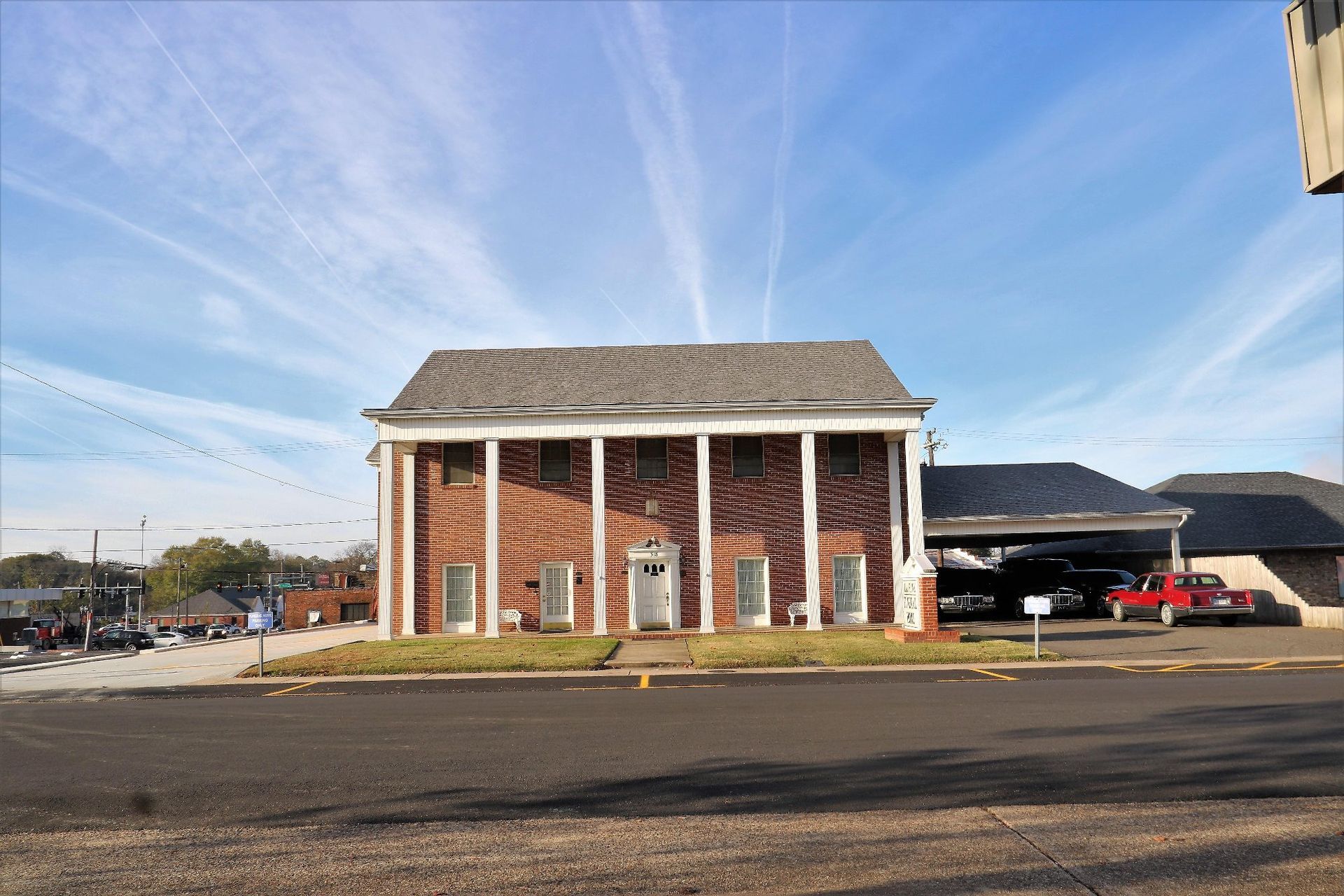 Brick building with white columns beside a parking lot under a blue sky