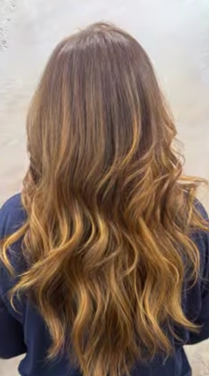 Vista posteriore di capelli lunghi e ondulati con una transizione di colore balayage tra castano caldo e caramello.