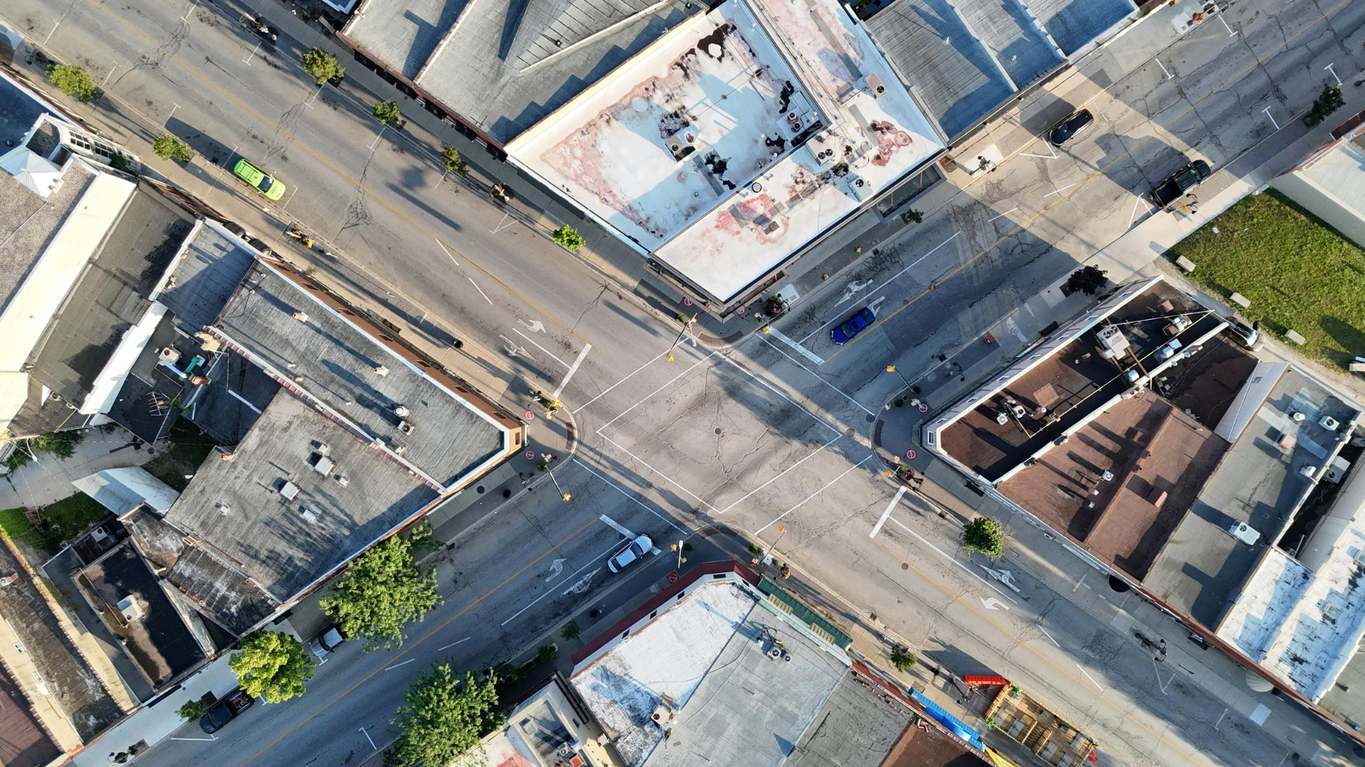 Aerial view of city intersection with buildings, cars, and crosswalks. Sunny day, shadows.