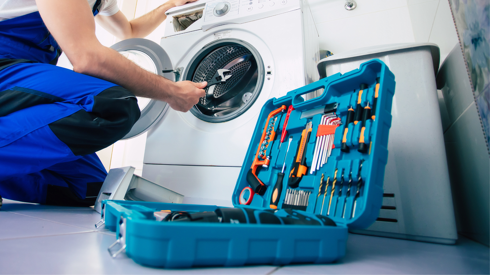 Repairman fixing washing machine; tools in an open case on the floor.