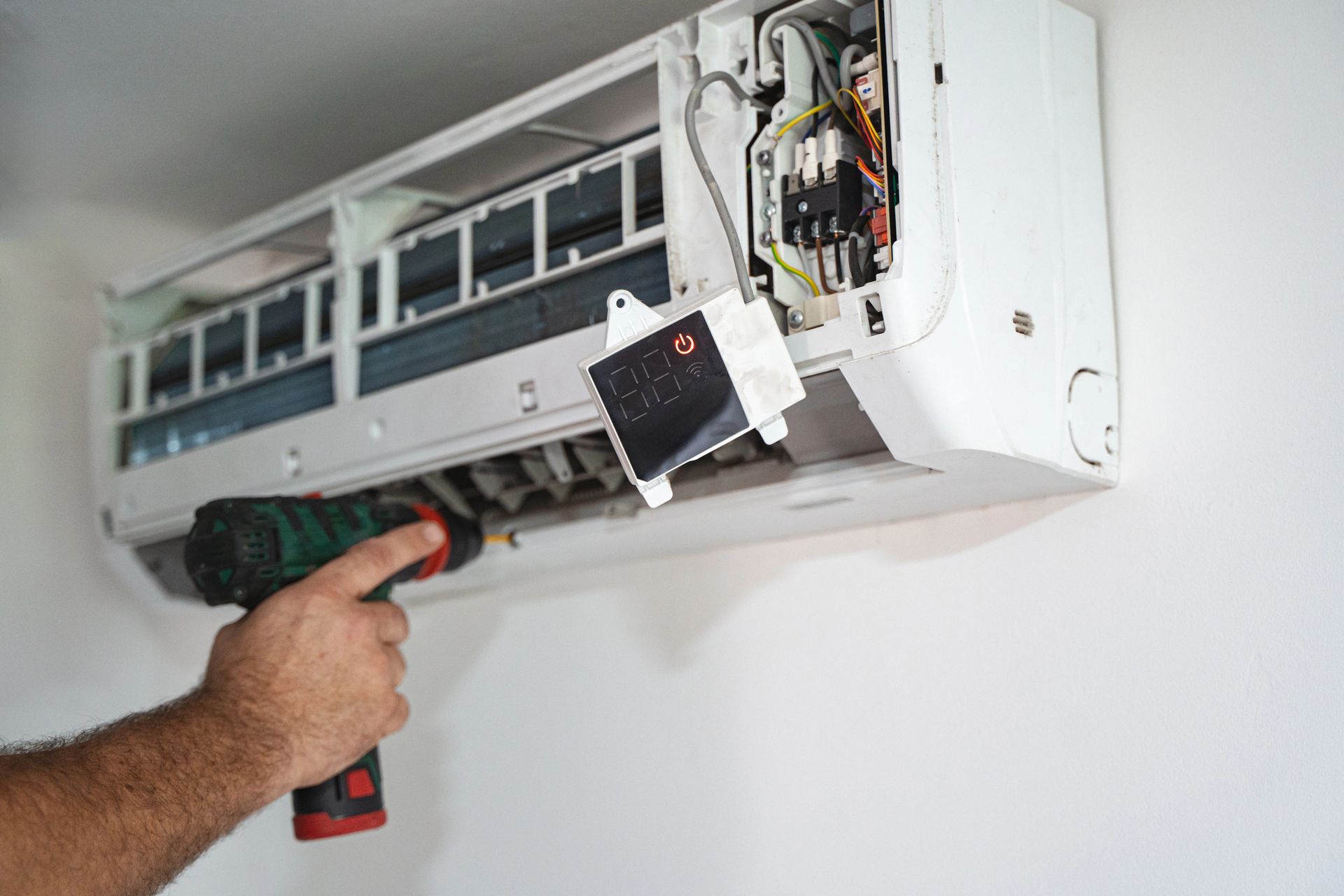 Técnico reparando un aire acondicionado de pared con herramientas y cableado expuesto.