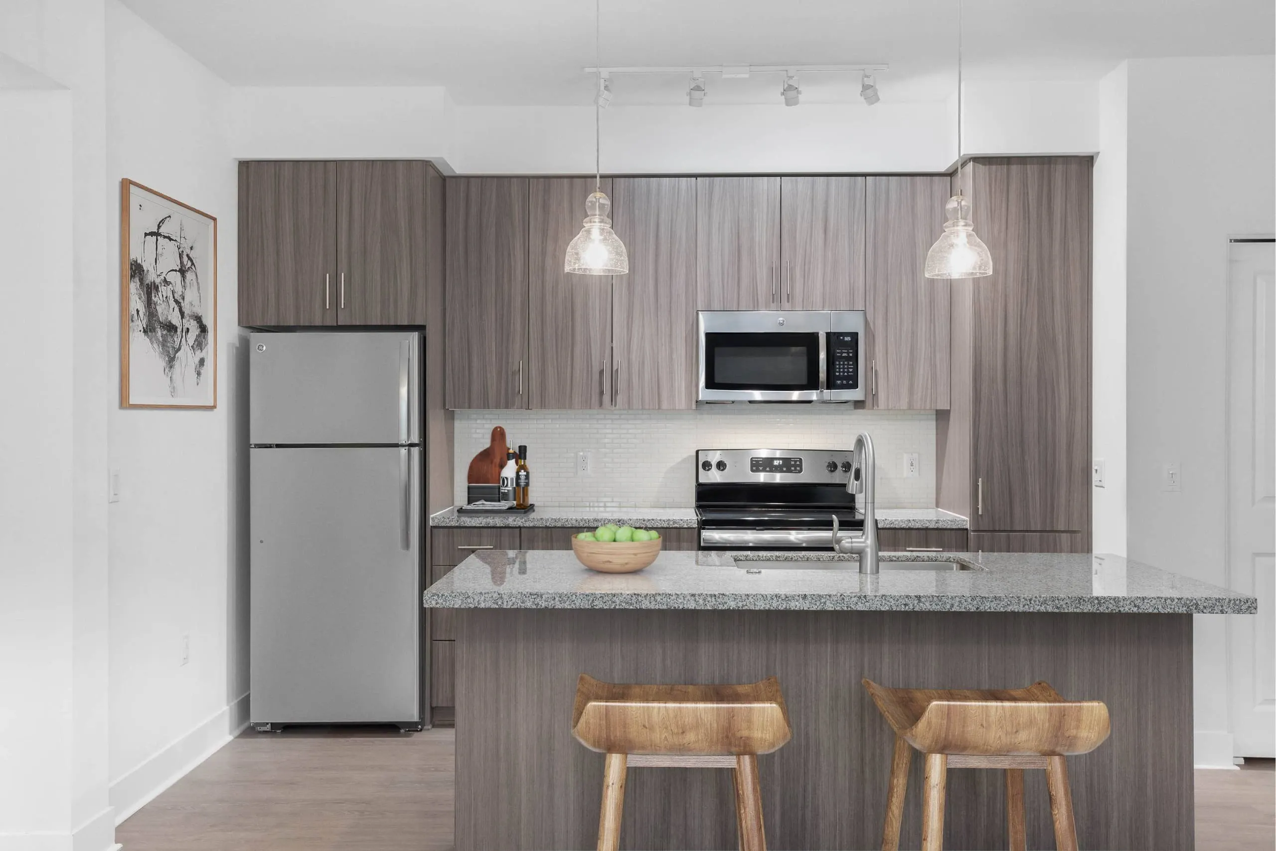 A modern kitchen with a refrigerator, microwave, oven, and a counter with two chairs at Cadia Crossing offers apartments in Gilbert, AZ.