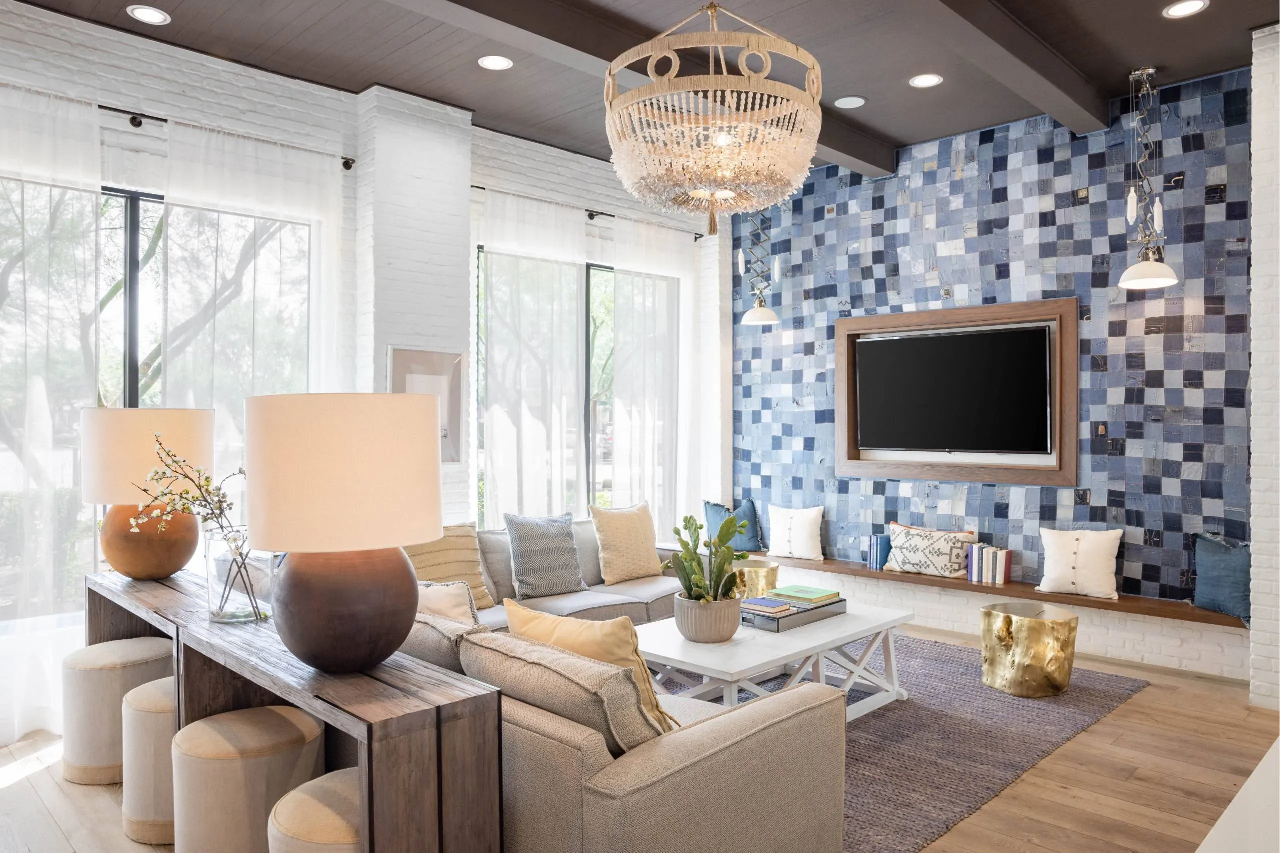 A modern clubhouse with a large sofa, a wooden coffee table, and a chandelier at Cadia Crossing offers apartments near downtown Gilbert, AZ.