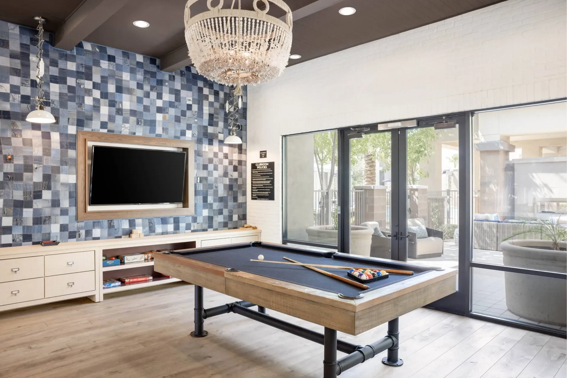 A pool table is in the middle of a room with a tv and a chandelier at Cadia Crossing offers apartments in Gilbert, AZ, near Gilbert Town Square.