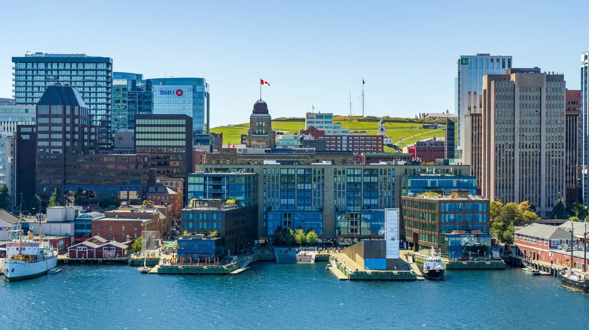 Harborfront city skyline with colorful waterfront buildings and boats on blue water under a clear sky