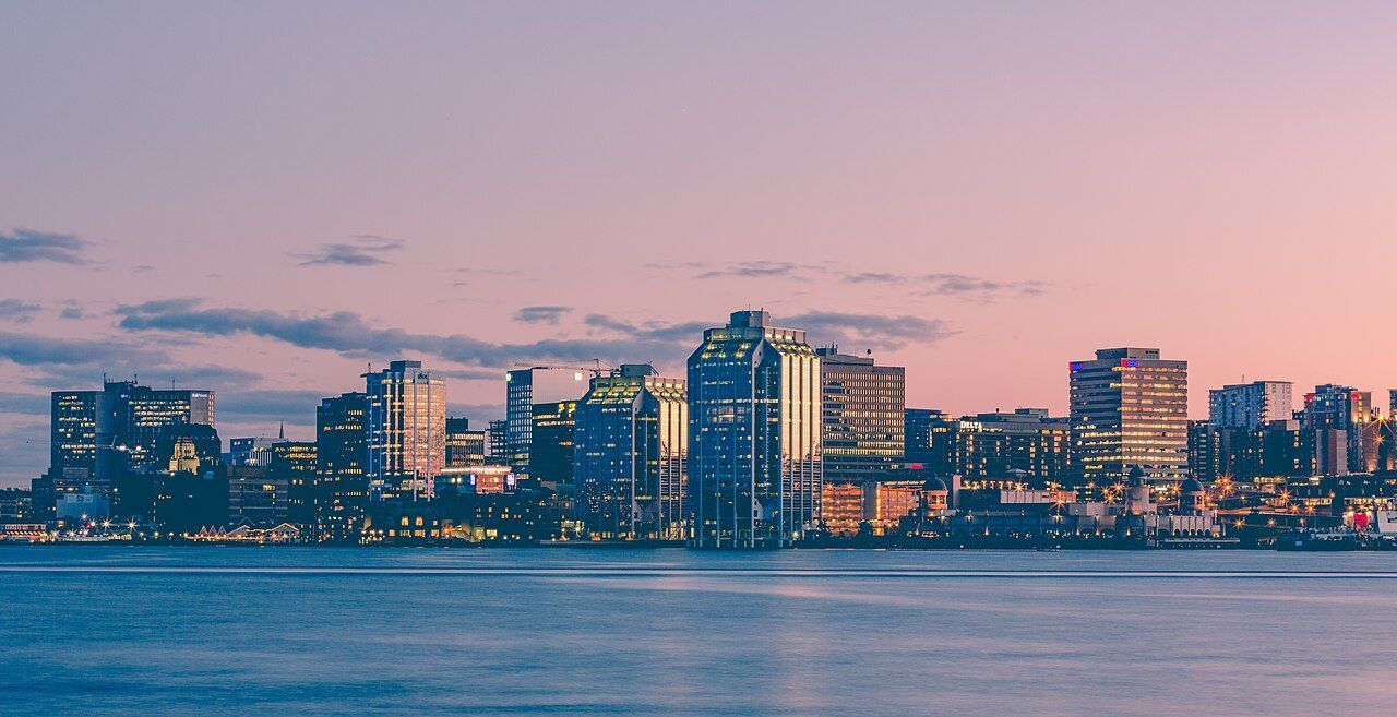 City skyline across calm water at sunset, with pink and blue sky and lit buildings.