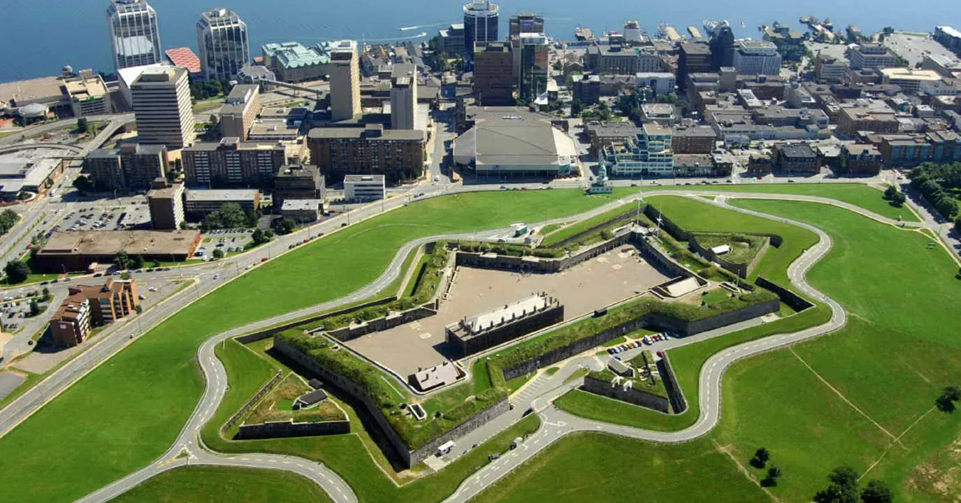 Aerial view of a star-shaped fort with green lawns beside a city waterfront.
