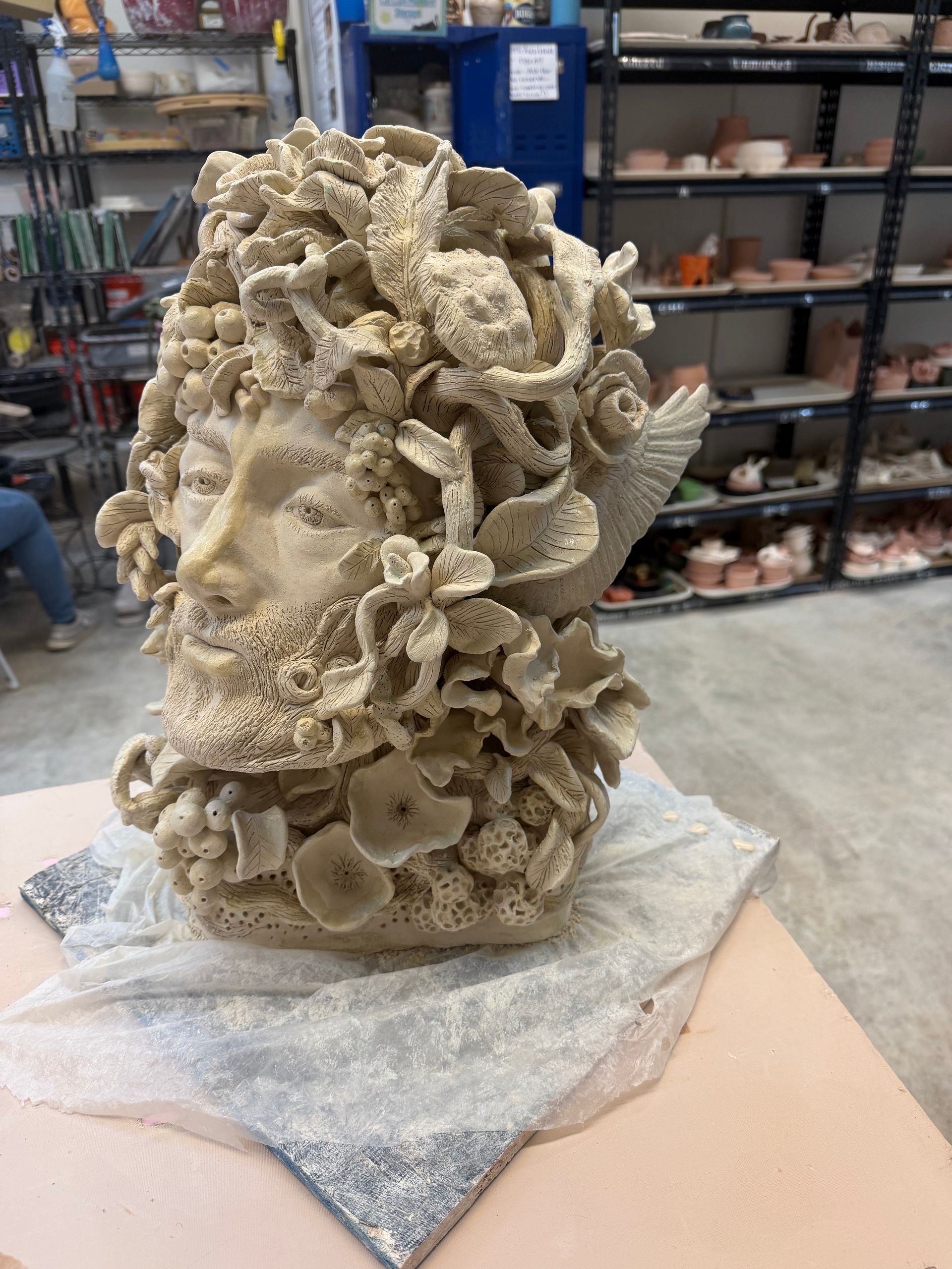 Stone sculpture of a face entwined with coral-like and shell forms in a workshop setting