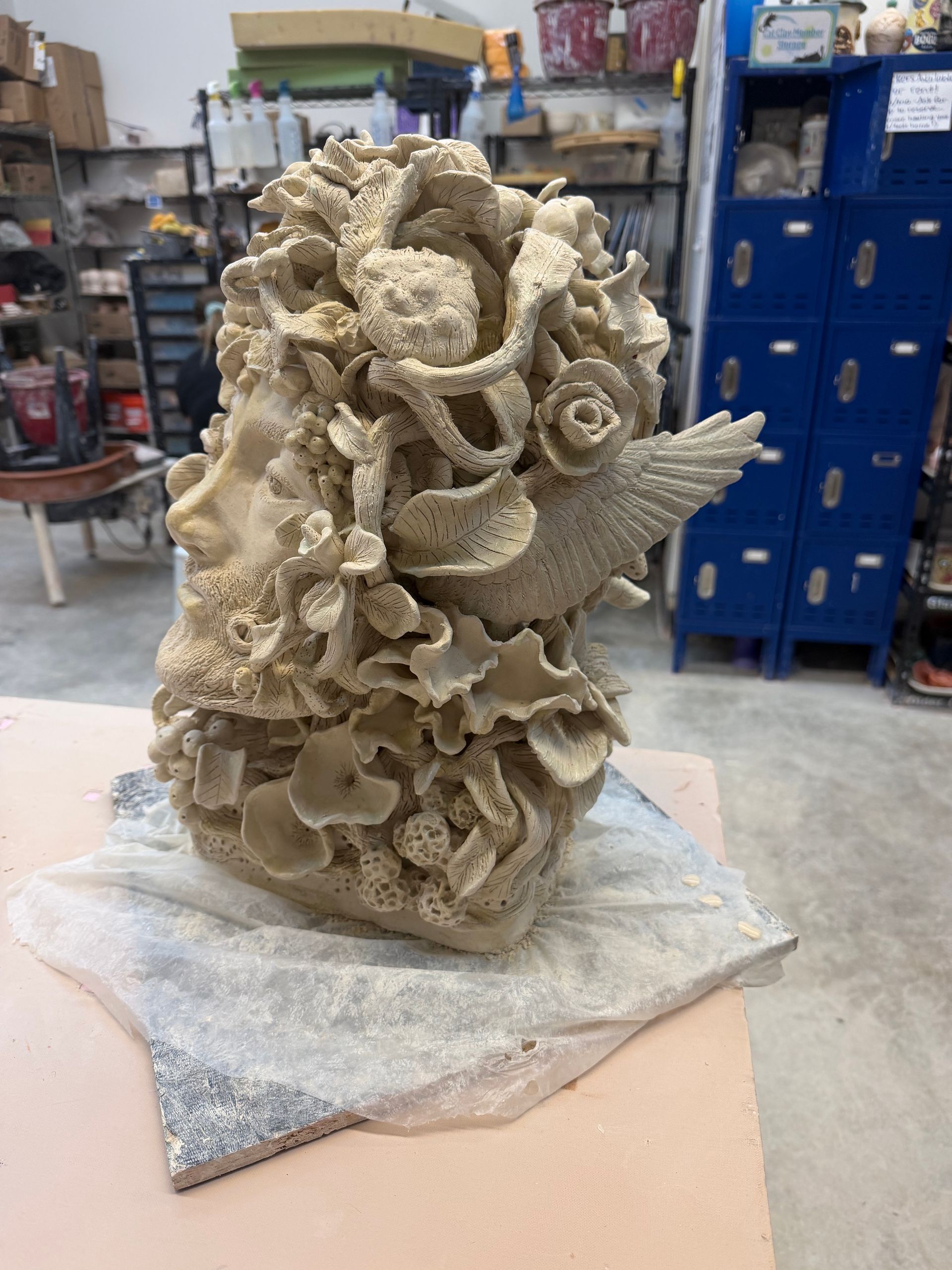 Intricate beige coral sculpture on a stone base in a workshop or storage area