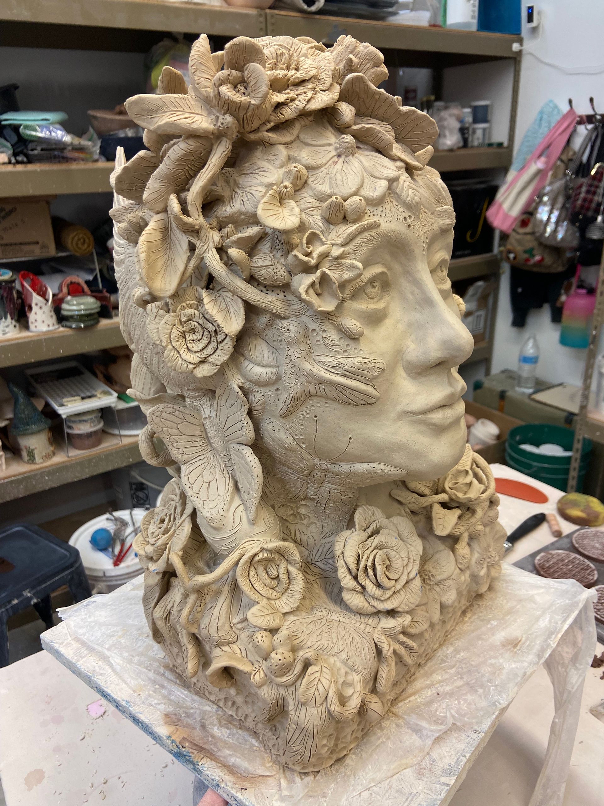 Cream-colored floral bust sculpture with a side profile face on a worktable in an art studio