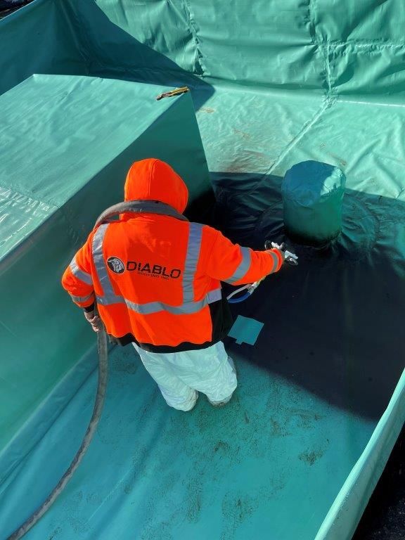 A man in an orange jacket is spraying something on a blue surface. | Oakland, CA | Diablo Roofing