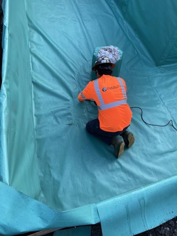 A man in an orange shirt is kneeling on a green tarp. | Oakland, CA | Diablo Roofing
