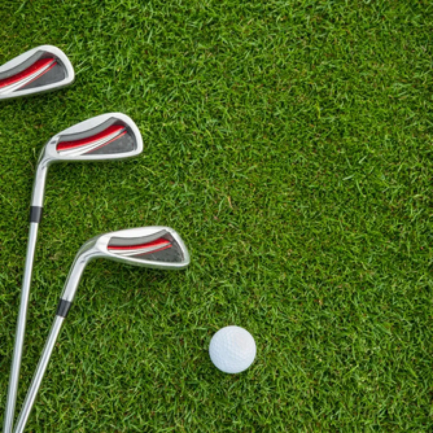 Three golf clubs and a white golf ball on green turf