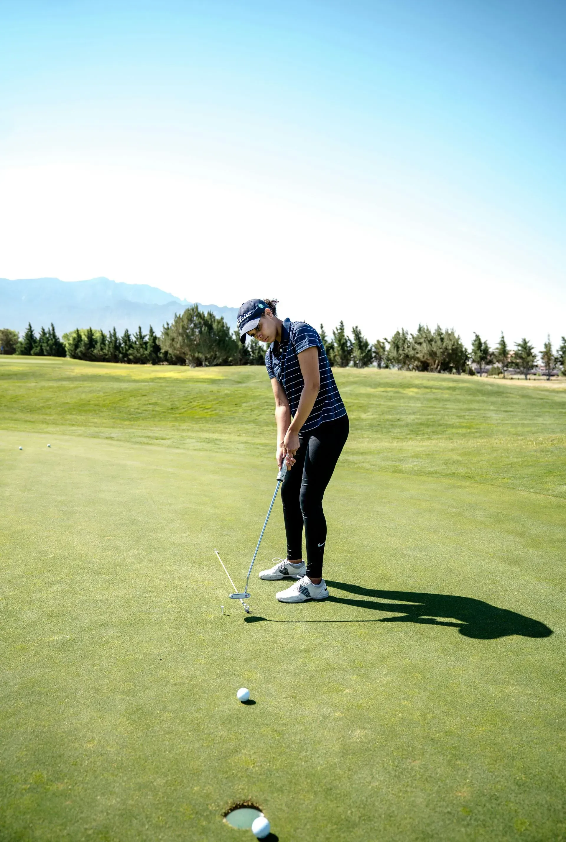 Golfer lining up a putt on a sunny green course with trees in the background