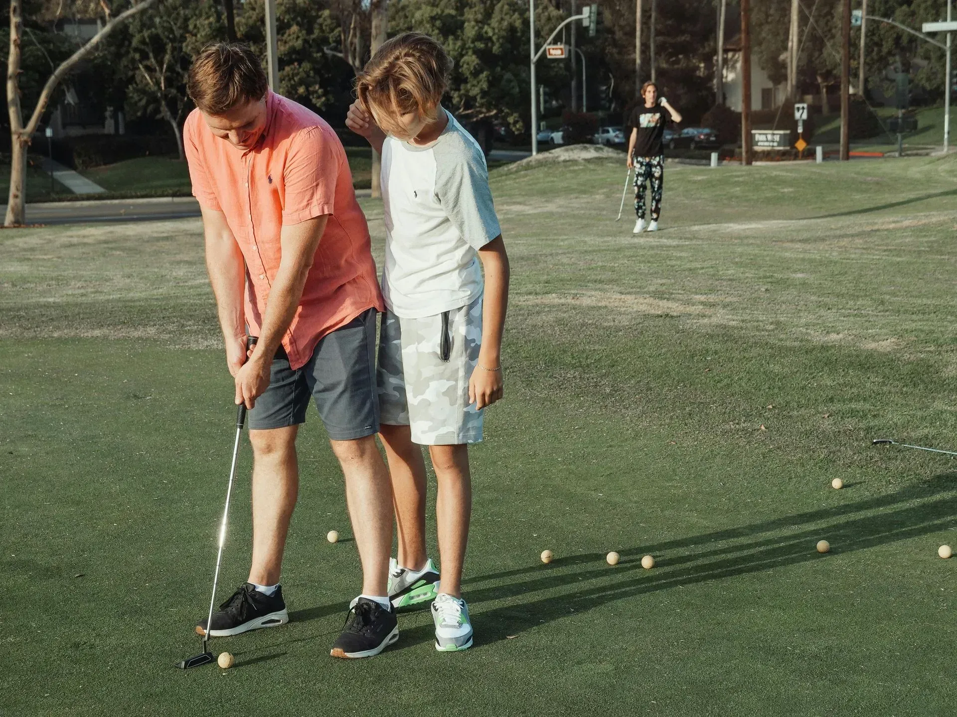 Two people practicing golf putting on a green under bright sunlight