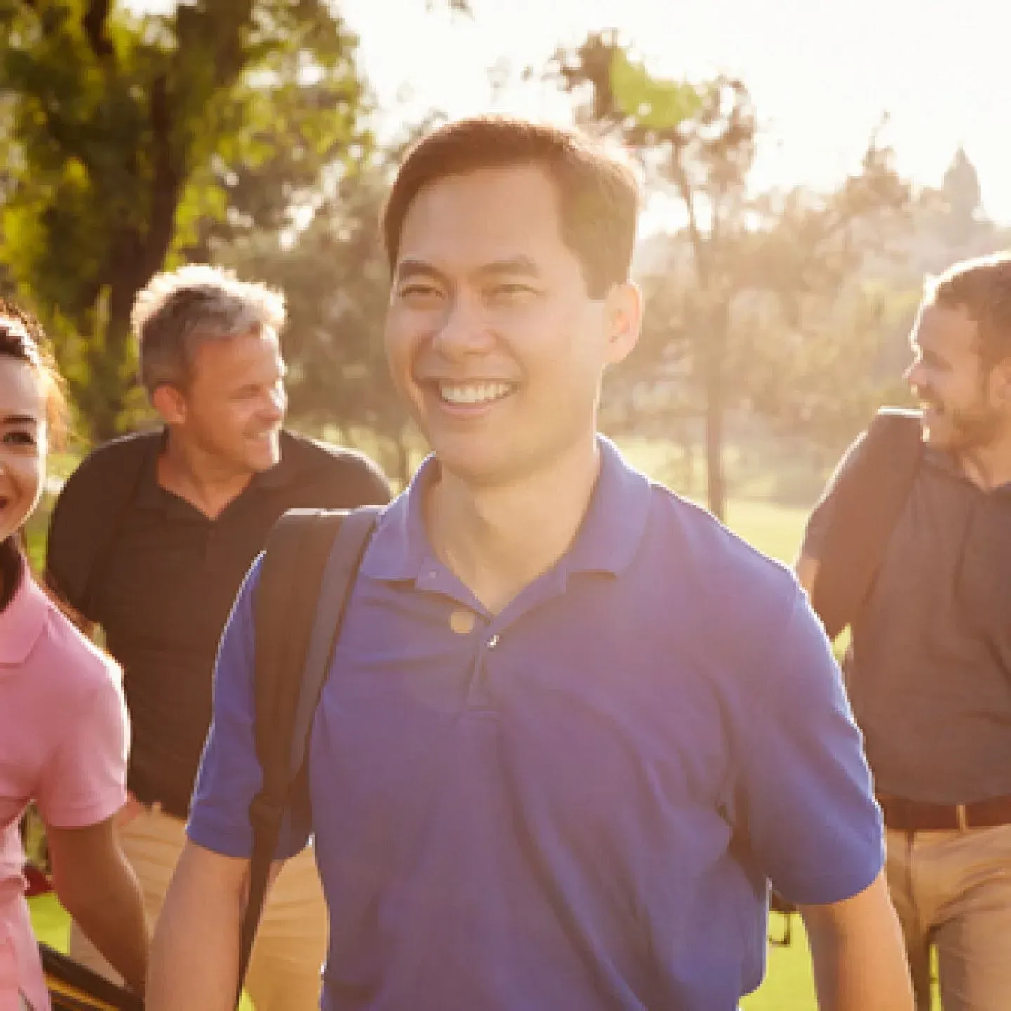 Group of coworkers walking outdoors in warm sunlight, smiling and chatting near trees.