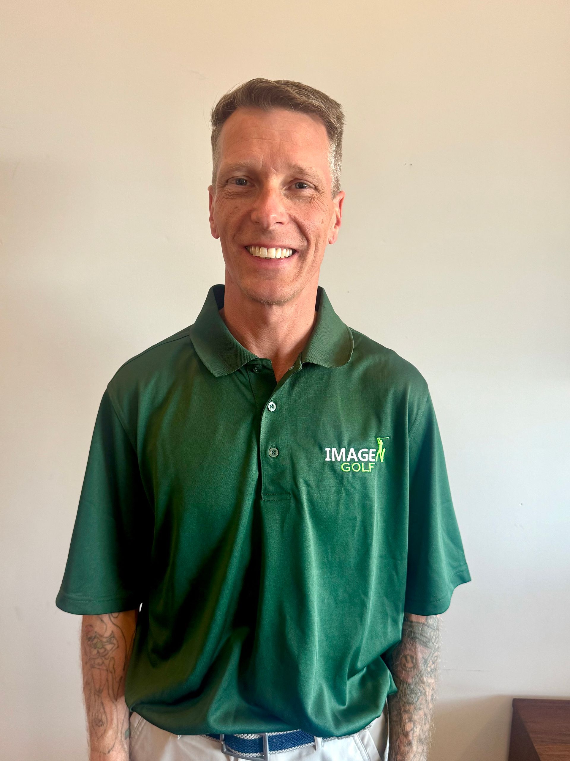 Smiling man in a green polo shirt standing against a plain wall