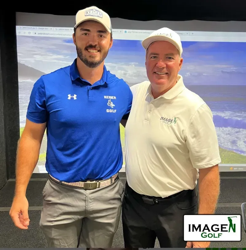 Two smiling men pose indoors in golf attire, standing in front of a golf course projection screen.