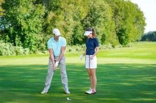 Two golfers standing on a green fairway, preparing to putt near a golf ball