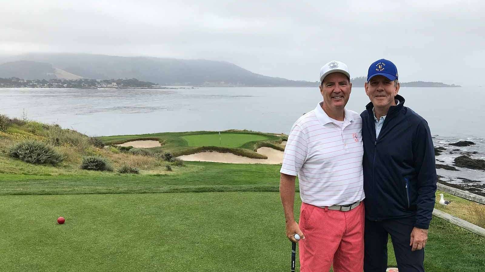 Two golfers standing on a green overlooking the ocean and distant hills