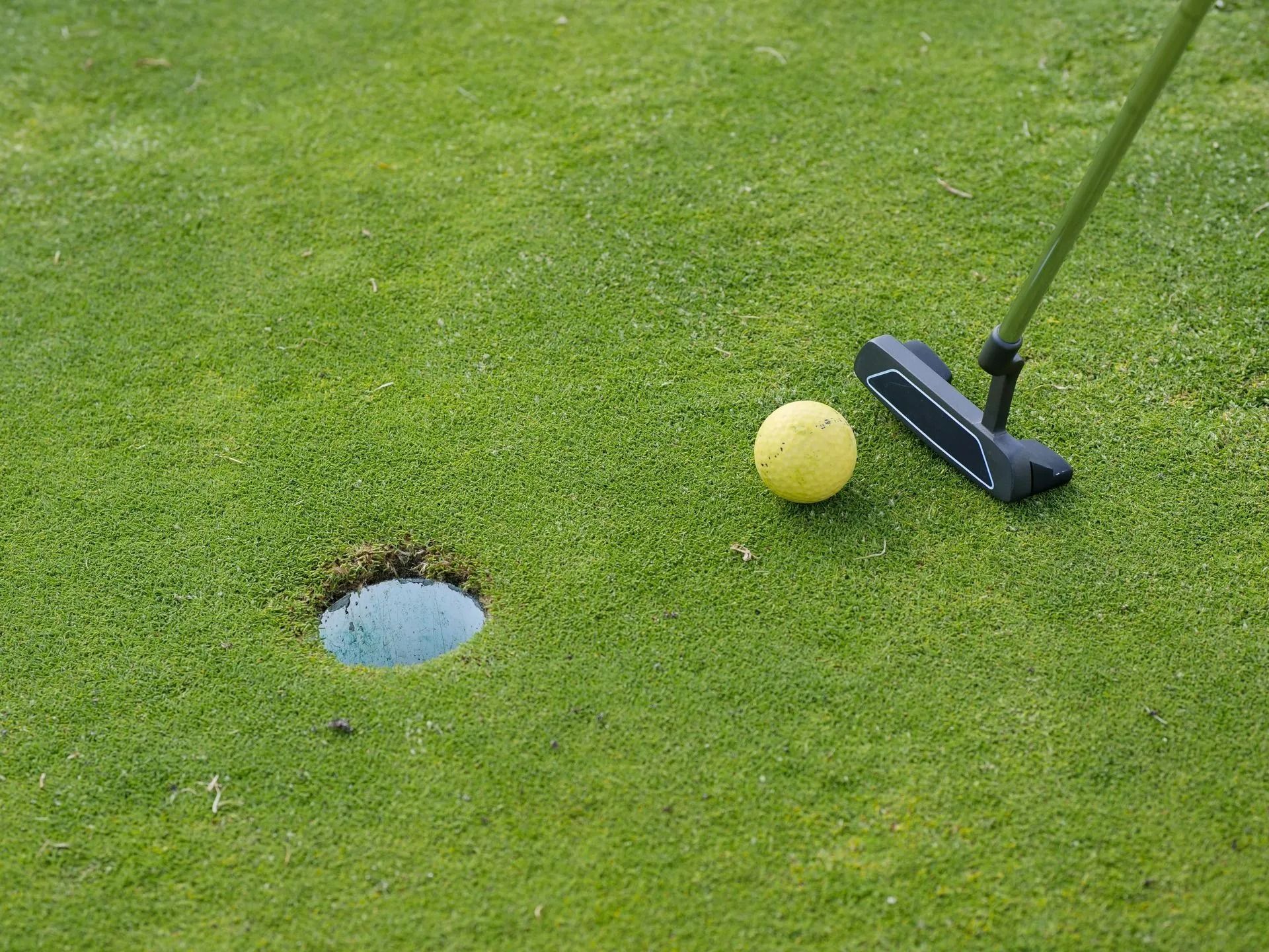 Golf green with a yellow ball near a putter and hole