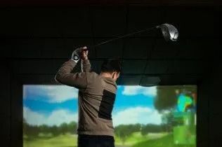 Golfer swinging a club at an indoor golf simulator screen