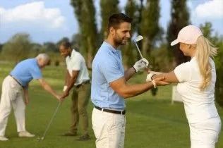 Golfers on a green shaking hands after a putt, with two others playing in the background.