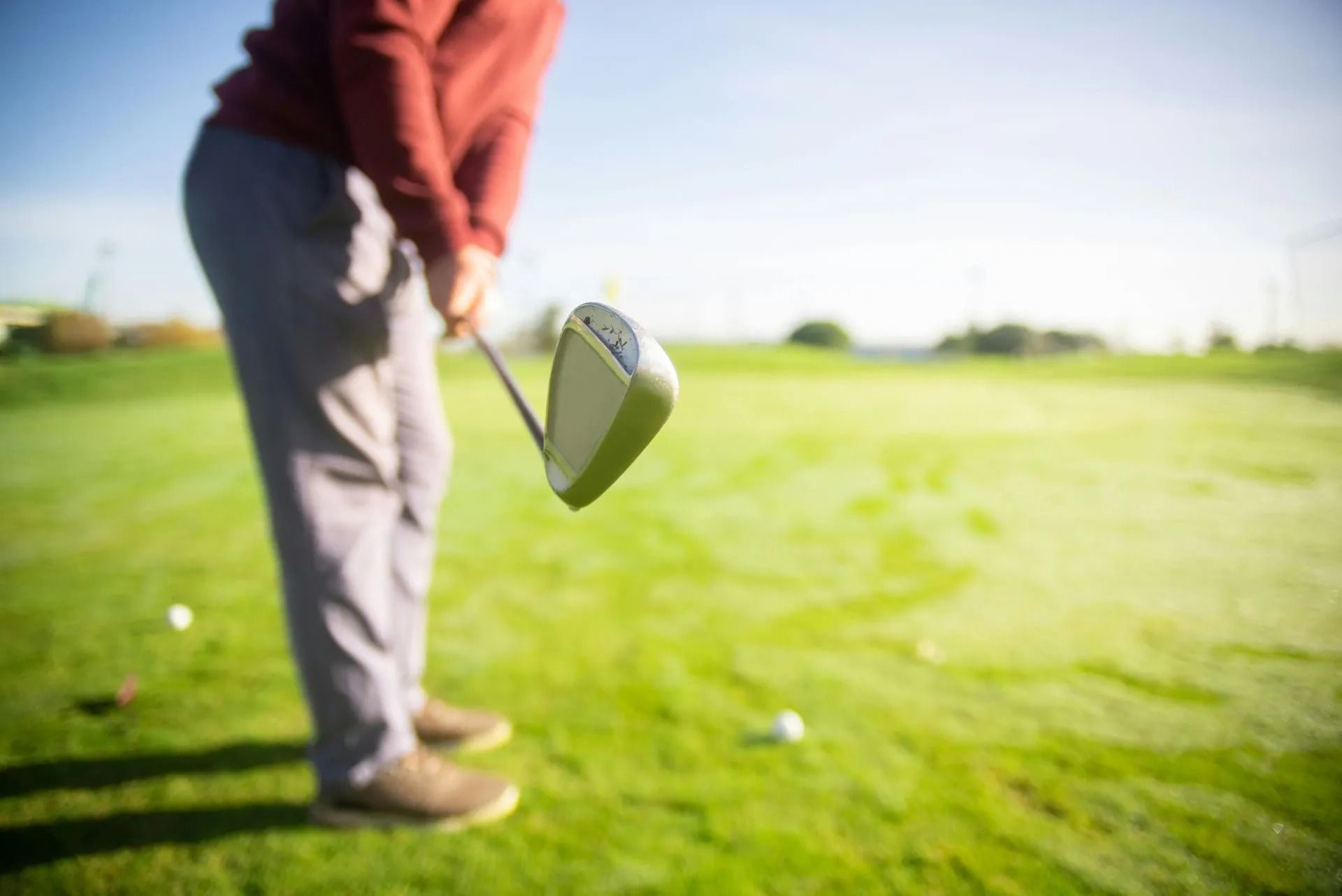 Golfer holding a club over a green golf course, with a ball in the foreground