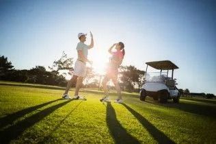 Two people dancing on a sunny golf course beside a golf cart, with long shadows on the grass.