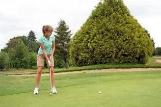 Golfer lining up a putt on a green with trees in the background