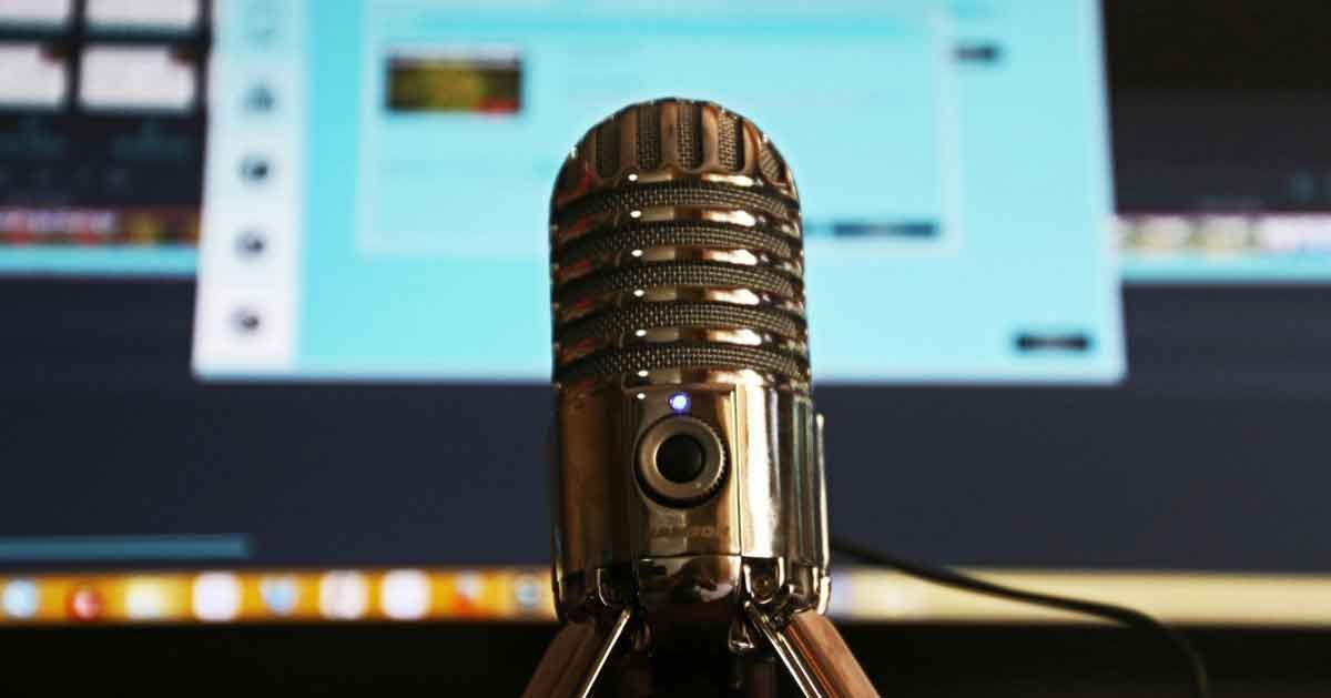 Close-up of a silver microphone on a desk in front of a blurred computer screen